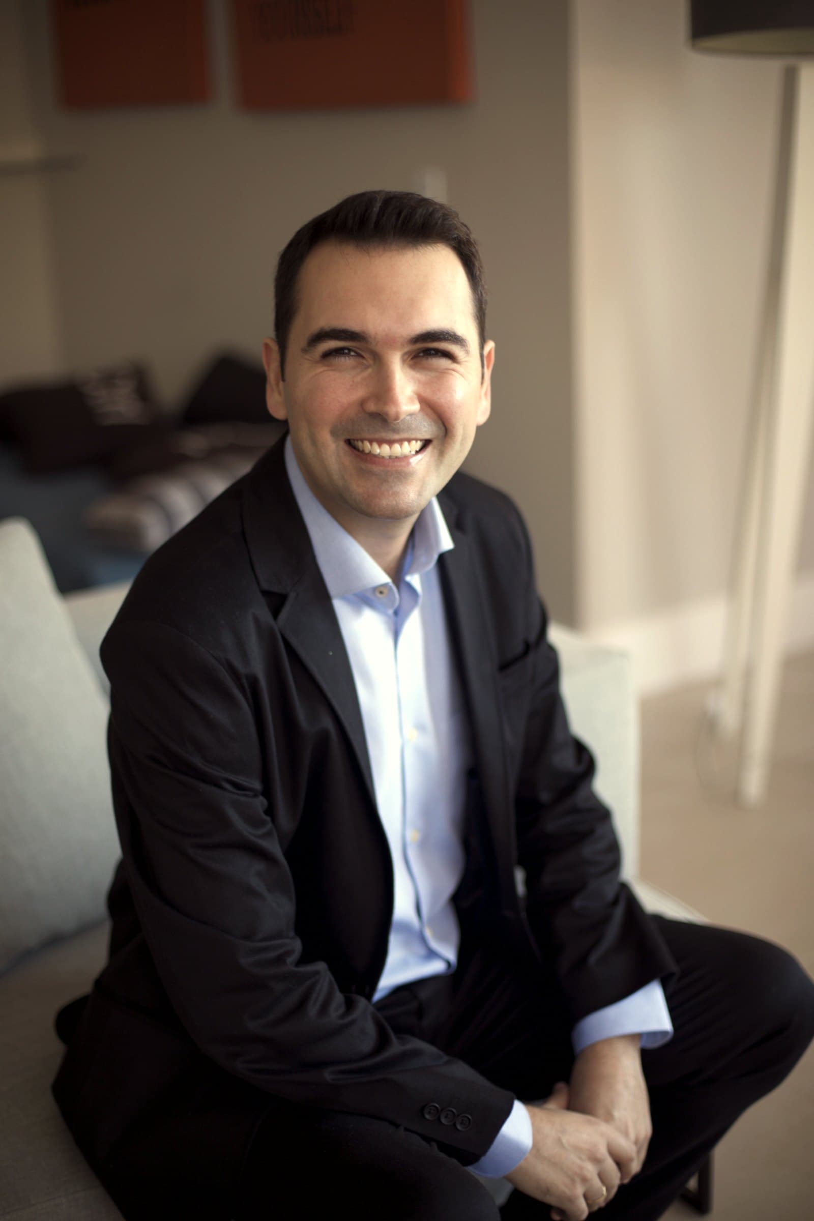 Júlio Domingos sentado, sorrindo, de blazer escuro e camisa azul